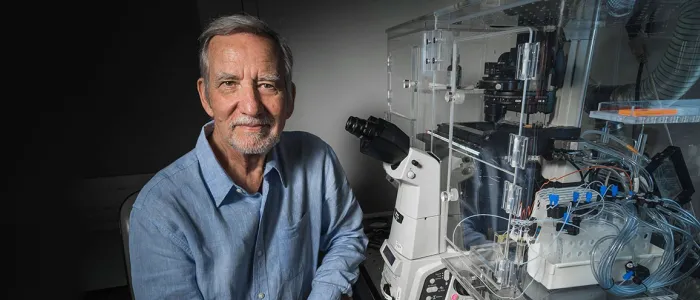 Photo of Professor Jim Spudich sitting in laboratory space next to a complicated microscope apparatus.