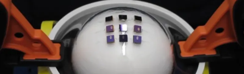 Screenshot image from video where test machine with orange clamps stretches translucent flexible electronic over a sphere.