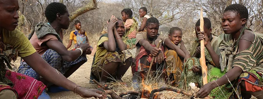 Photo of several members of the Hazda hunter-gatherer tribe in Tanzania crouched around a fire.