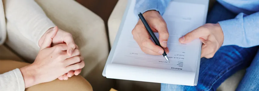 Photo of patient and therapist's hands during a meeting, therapist writing on a clipboard.