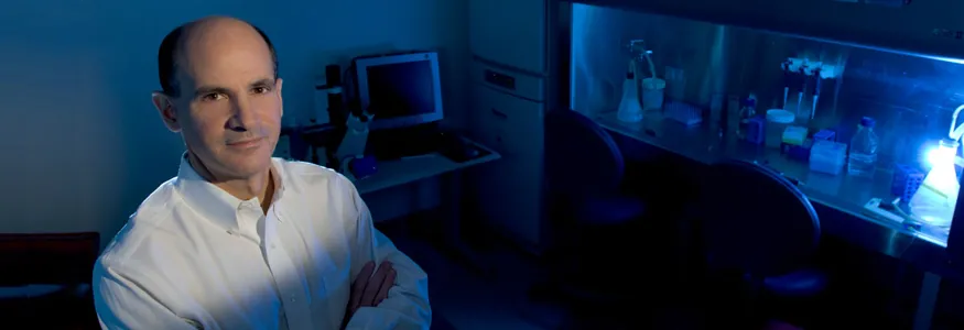 Photo of Dr. Thomas Rando in the laboratory, with fume hood lit up blue in the background.