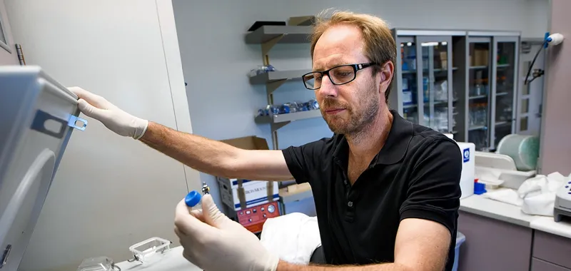 Photo of Dr. Tony Wyss-Coray examining a small test tube sample taken out from a centrifuge in the laboratory.