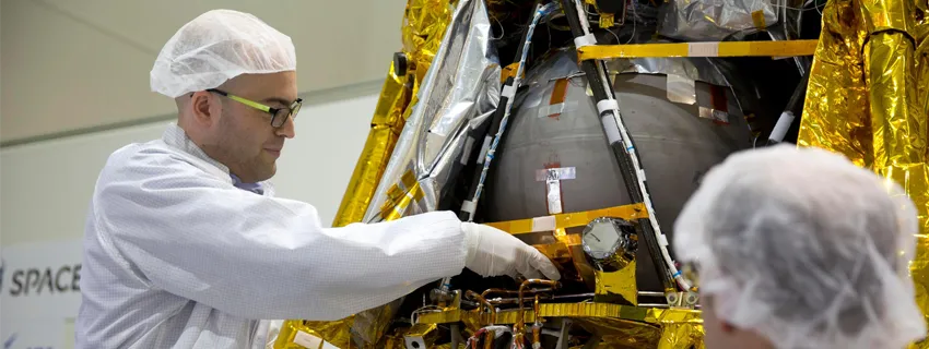 Photo of Stanford Bio-X Fellow graduate student Yonatan Winetraub inserting an object into a spacecraft, wearing protective clothing.