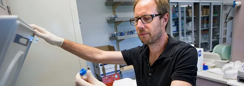 Photo of Dr. Tony Wyss Coray lifting a vial out of a piece of equipment in the laboratory.
